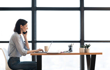Aufkleber - Corporate Communication. Happy female manager talking on mobile phone working on laptop in modern office, side view