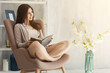 © Prostock-studio - Happy woman reading book by the window on spring morning
