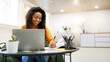 © Prostock-studio - Smiling young black woman sitting at desk working on laptop taking notes in notebook, happy millennial female study watching webinar using computer writing check list, banner panorama, free copy space