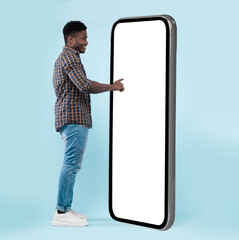Poster - Full Body Length Back View Of Black Man Using Big Smartphone With Blank White Screen Touching Huge Display Panel With Finger, Cheerful Guy Standing On Blue Background, Ordering Food Delivery, Mock Up
