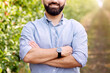© Prostock-studio - Confident owner of eco farm, work outside, successful business and growing orchard. Friendly smiling bearded young man with crossed arms on chest on path on plantation with green apple trees in garden