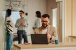 © Zamrznuti tonovi - Businessman making video call on laptop in coworking space with colleagues discussing in background