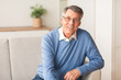 © Prostock-studio - Happiness In Old Age. Positive Elderly Gentleman Smiling Looking At Camera Sitting On Sofa At Home.