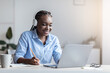 © Prostock-studio - Black Female Office Employee Watching Webinar On Laptop At Workplace And Taking Notes, Wearing Headphones, Free Space