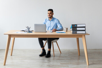 Poster - Portrait Of Smiling Middle Eastern Male Manager Working On Laptop Computer In Modern Office, Cheerful Guy Sitting At Desk And Using Pc, Looking At Screen Watching Webinar, Free Copy Space