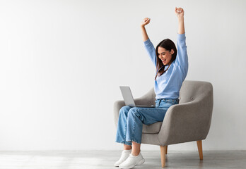 Poster - Overjoyed millennial woman sitting in armchair with laptop, celebrating huge online win or success against white studio wall, copy space. Young lady enjoying big sale in web store