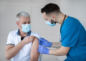 Poster - Professional doctor or nurse giving COVID-19 vaccine injection to senior patient at clinic. Mature man in face mask getting antiviral vaccine at health center during immunization campaign