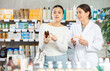 © JackF - Asian woman buyer choosing medicinal cough liquid syrup standing between shelves at big pharmacy, young girl pharmacist consulting customer