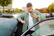 © maxbelchenko - A handsome man in glasses with a phone stands near his car in a parking lot. A stylish man near a car enjoys the sunset with a phone. Transportation, leisure concept.