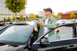 © maxbelchenko - A handsome man in glasses with a phone stands near his car in a parking lot. A stylish man near a car enjoys the sunset with a phone. Transportation, leisure concept.