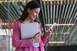 © Westend61 - Young businesswoman holding laptop while using mobile phone by glass wall