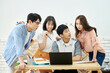 © Dialogue Frame - Young Asian Men and Women Collaborating on Project Around Laptop in Modern Study Room