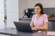 © anatoliycherkas - Young woman working from home using laptop in kitchen