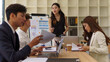 © matinee - Businesswoman giving a team presentation with charts and data visuals in a bright modern office.
