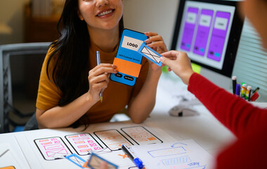 two young female web designers adding an email icon to a mobile app prototype during a brainstorming