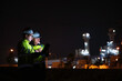 © reewungjunerr - Industrial engineer night inspection at refinery or petrochemical plant walkie-talkie hand and digital tablet intersection of technology, worker work at night at power plant