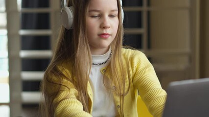 Aufkleber - Close-up of a girl with straight hair wearing headphones and a yellow cardigan. She gently touches the headphone as she is listening to music. The background features a neutral-toned room.
