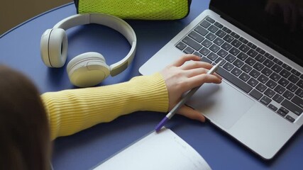 Aufkleber - A student types on a laptop, with a pen in hand. Headphones and school supplies on the table. The scene suggests remote work, school, or online learning in a study or home environment.