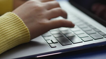 Poster - Close-up of hands typing on a sleek, modern laptop. The focus is on the keyboard and the person's hands, which are in motion as they type. A yellow sweater sleeve is visible.