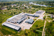 © Raivo - Aerial view of a rural industrial zone near a small town and lake, with warehouse buildings, roads, fields, and surrounding residential areas..