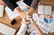 © Pixel-Shot - Business team putting hands together as symbol of unity during meeting in office, closeup