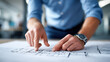 © INT888 - Person blue shirt is pointing architectural plans table, indicating specific details with their finger, while other hand rests plans. setting appears to be office or design studio, with focus