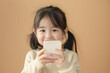 © Surachetsh - Little girl holding up a smartphone and smiling brightly in a white dress on beige background.