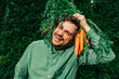 © VISTA by Westend61 - Man in green shirt holding carrots over his head and smiling outdoors
