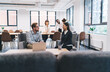 © BullRun - Young professionals relaxing in shared lounge after business meeting, checking phones and reviewing notes, combining modern casual work culture with thoughtful follow-up in creative office space