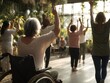 © TesaI - Senior woman in wheelchair practicing gentle arm yoga poses with diverse group in inclusive class