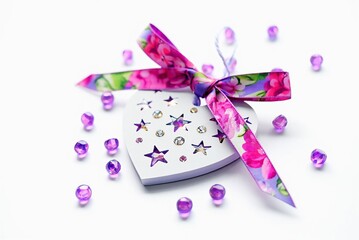 Aufkleber - A heart-shaped box of chocolates adorned with purple beads and a bow on top, surrounded by an assortment of purple beads.