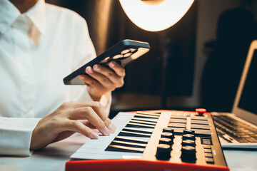 Poster - Pianist Concept. Close-up of a person using a smartphone while playing a musical keyboard in a cozy home setting