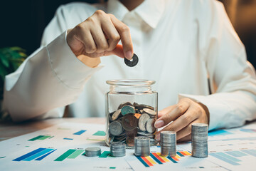 Poster - Concept of saving money. Woman Investing Coins into Glass Jar in Financial Planning Concept with Charts and Tables on Table