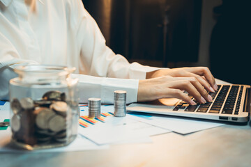 Poster - concept of saving money. businessperson working on laptop with coins and financial reports on table 