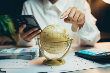 Poster - Business concept. Business Professional Analyzing Globe and Data on Table with Smartphone and Calculator in Modern Office Setting