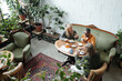 © pressmaster - Overhead view of people sitting at round table, drinking coffee and conversing in cozy cafe with green plants and vintage furniture