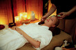 © InfiniteFlow - Serene ambiance of spa salon, woman customer indulges in rejuvenating with luxurious face cream massage with warm lighting candle. Facial skin treatment and beauty care concept. Quiescent