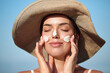 © verona_studio - Woman applying sunscreen to her face. . Skincare. Body Sun protection.  Female in hat smear moisturizing lotion or sun cream on skin.