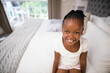 © wavebreak3 - African American child girl smiling while sitting on bed near window with garden view