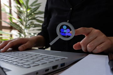 Poster - Businesswoman working on her laptop, while pointing at a magnifying glass simple 3D icon analyzing a group