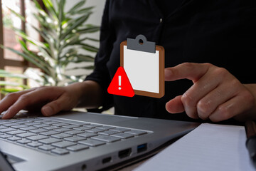 Poster - Businesswoman working on her laptop, while pointing at a simple 3D icon of a clipboard with a warning sign