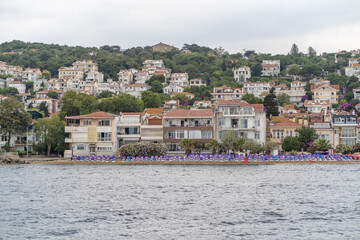Aufkleber - Beautiful coastal view of Prince Islands showcasing homes and beach umbrellas on a cloudy day with lush greenery in the background