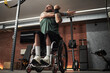 © DragonImages - Individual with tattoos working out in gym, using resistance bands while sitting in wheelchair. Equipment and devices visible in background