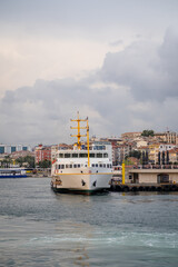 Aufkleber - Bosphorus ferry docked at the waterfront surrounded by city buildings on a cloudy day