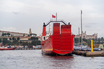 Poster - Bosphorus harbor with red cargo ship docked near historical buildings during overcast day