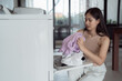 © Tj - Young woman inspecting freshly laundered clothes after using the washing machine at home, enjoying the satisfaction of completing daily chores and maintaining a tidy living space