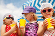 © yanlev - Little girls in bathing suits drinking sweet drinks from a straw under a sun umbrella