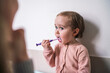 © Studio Marmellata - A cute toddler is brushing their teeth with a purple toothbrush. This young child practices good dental hygiene habits in the bathroom during their daily routine.