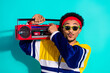 © deagreez - Energetic young man in retro sportswear holding a vintage boombox against a vibrant teal background