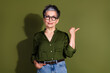 © deagreez - Confident mature woman in green shirt and glasses making a pointing gesture against a matching olive background